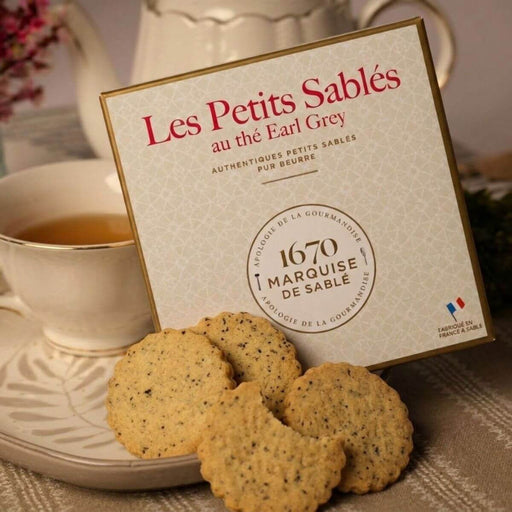 Box of 'Les Petits Sablés au the Earl Grey' cookies with a cup of tea on a table.