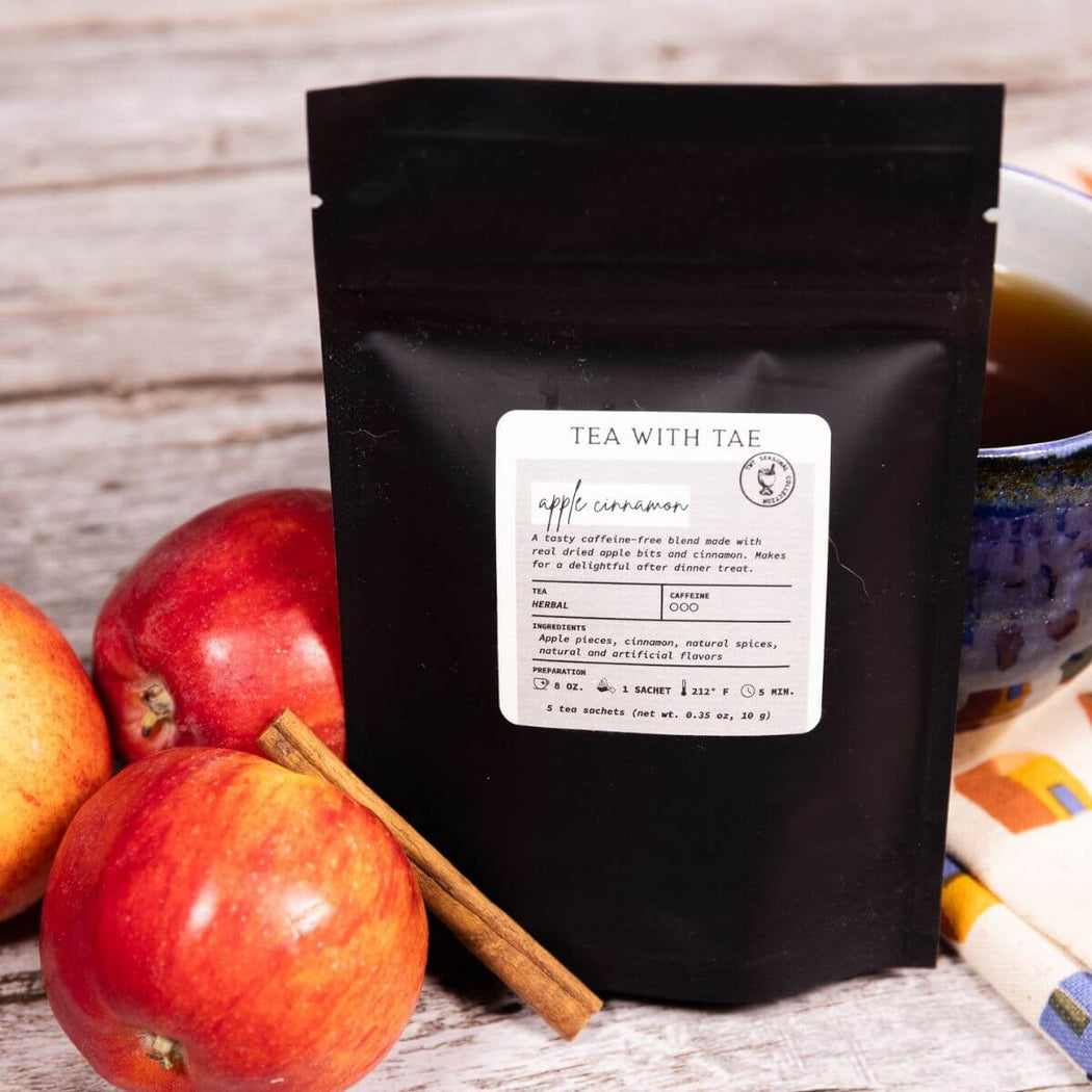 Black tea packaging with apples and cinnamon on a wooden surface