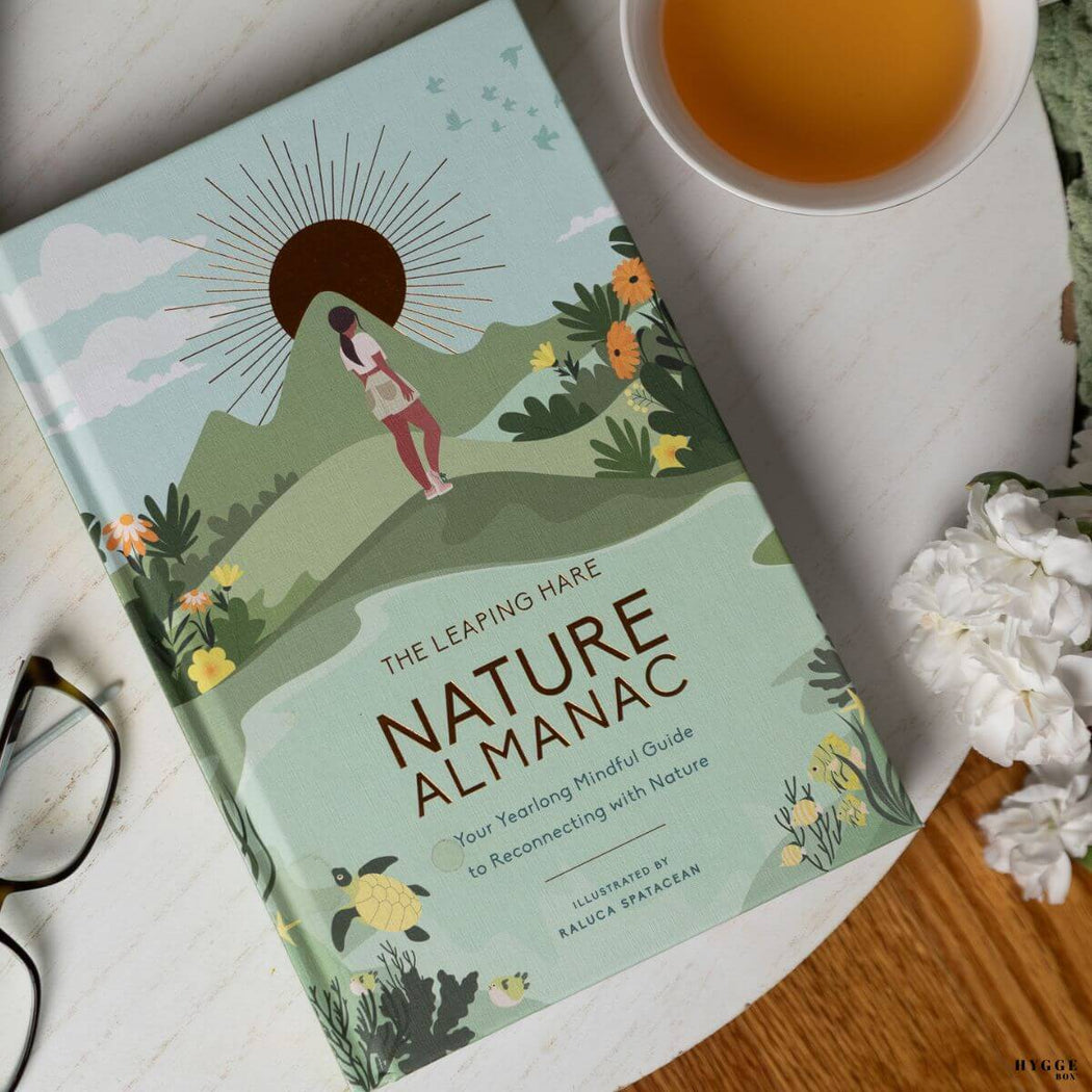 Book titled 'Nature Almanac' on a table with a cup of tea and glasses.