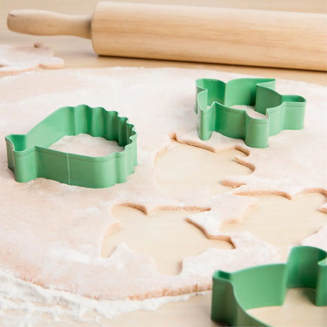 Sage green metal cookie cutters shaped like a turle, fish and shell, shown on a floured surface with a wooden rolling pin in the background.