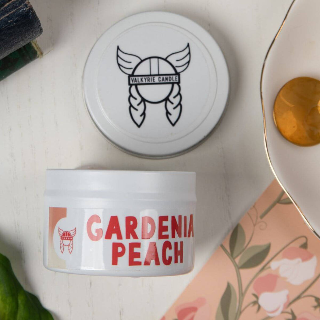 Gardenia Peach Valkyrie Candle in a white jar with matching lid, styled beside a floral card and warm-toned decor.