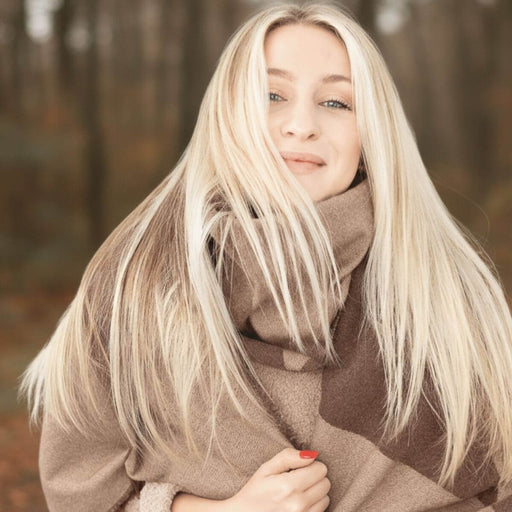 Woman with long blonde hair wearing a brown scarf in a forest setting.