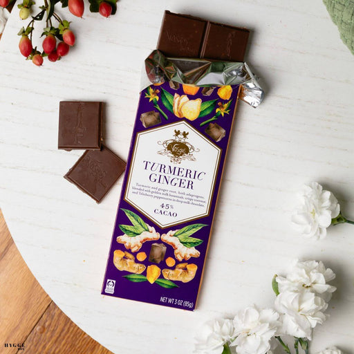 Turmeric Ginger chocolate bar packaging on a white surface with flowers and chocolate pieces.