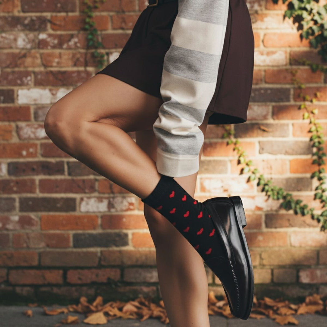 Woman wearing heart print socks standing in front of a brick wall background.
