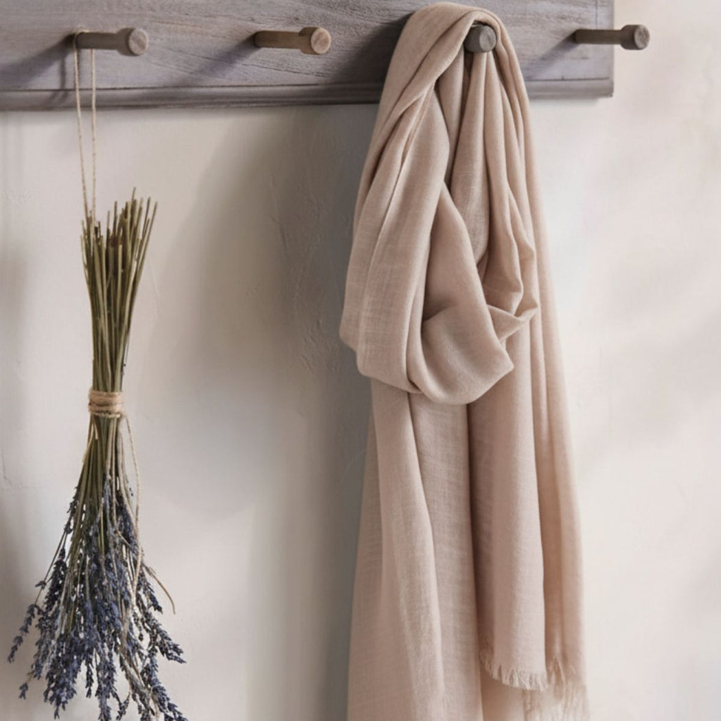 Beige women's lightweight wrap hanging on a wooden rack with a bundle of lavender against a neutral wall.
