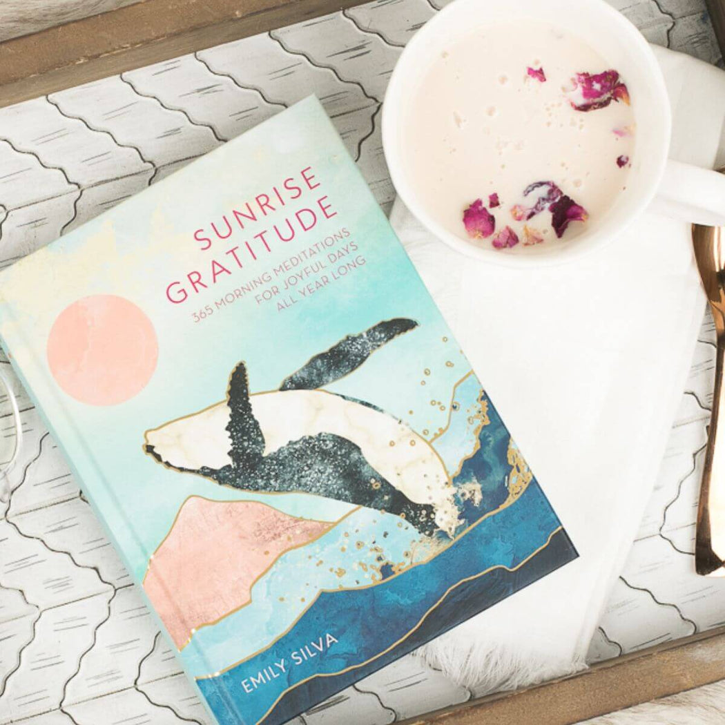 Book titled 'Sunrise Gratitude' by Emily Silva with a beverage on a textured surface