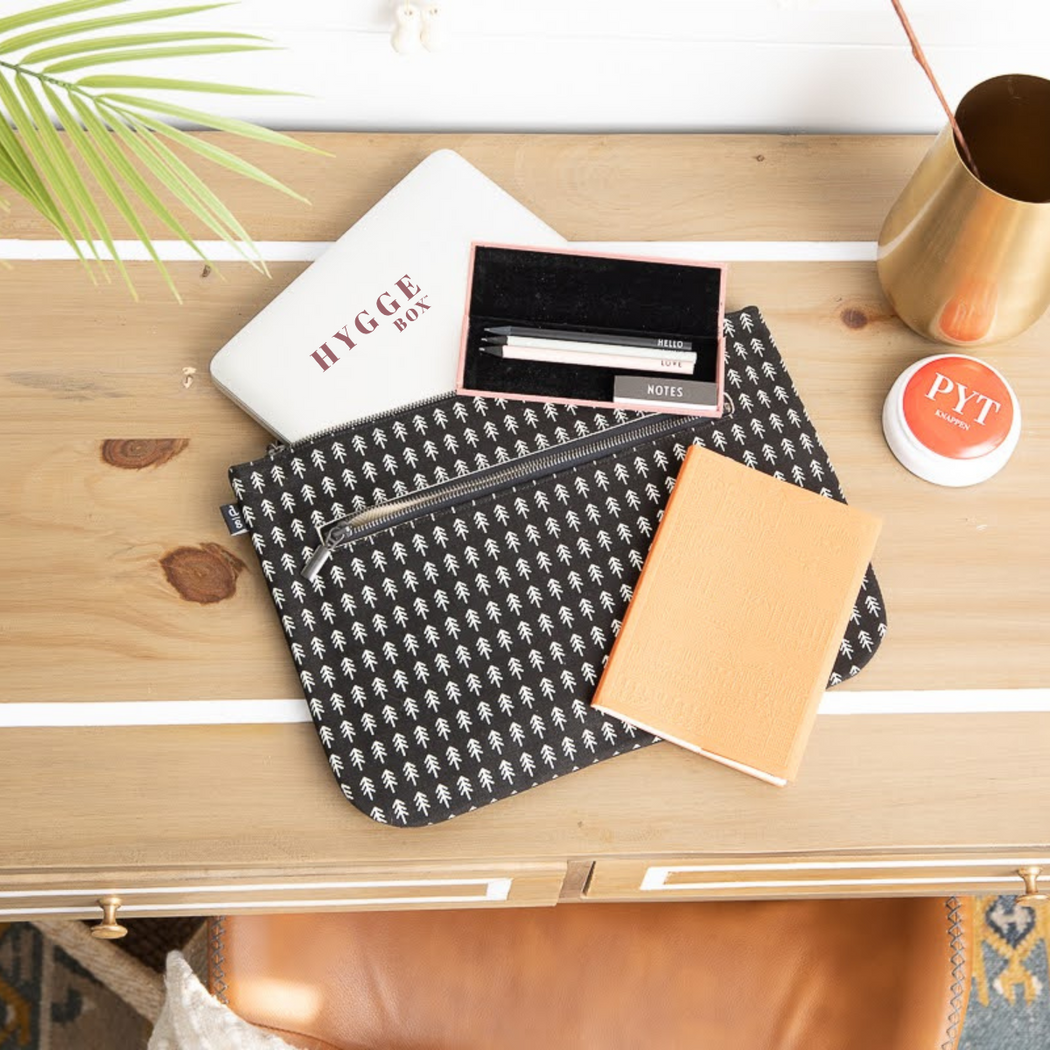 A wooden desk with office supplies - laptop, pencils, a cotton folio, a notebook and a pyt button.